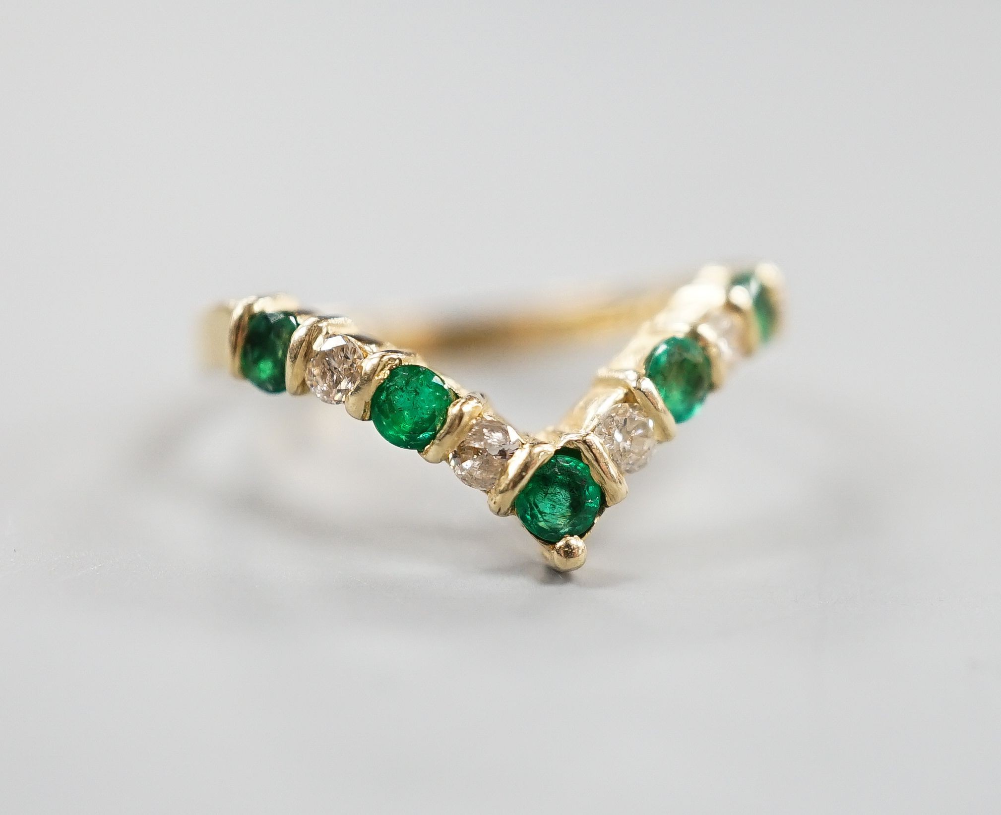 A modern 14k yellow metal, five stone emerald and four stone diamond set wishbone ring, size M, gross 2.3 grams.